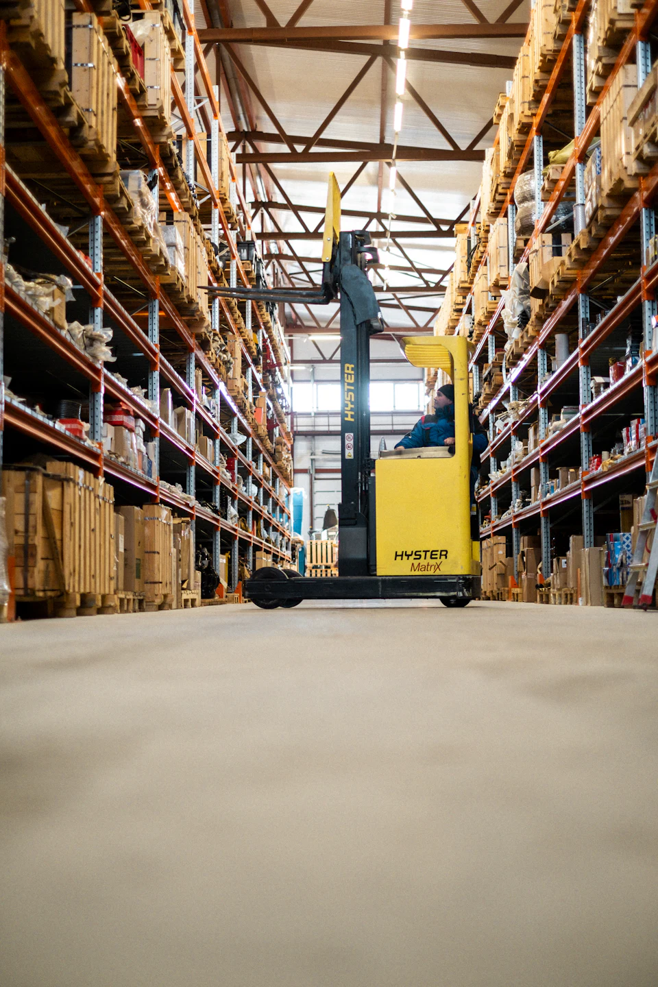 A worker operating a yellow forklift between warehouse storage racks.